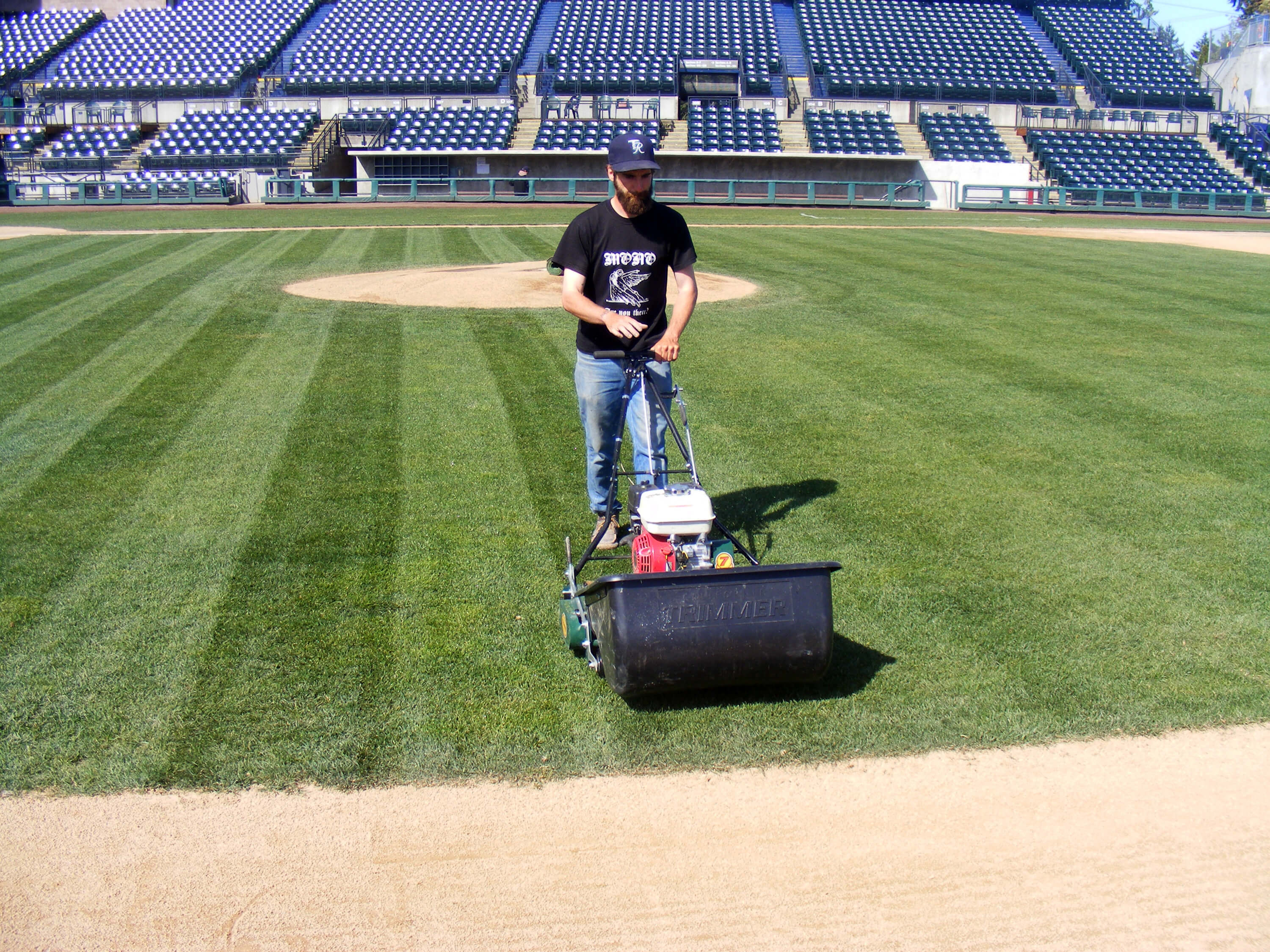 man mowing straight lines on a baseball field using a bucket attachment on the mower